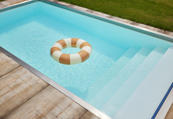 Piscina rectangular con agua azul, terraza de madera y flotador en Unbrick One lodge en los Países Bajos.