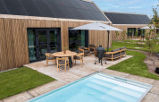 Modern wooden lodge at Brinckerduyn, Netherlands, with terrace, pool, garden furniture, and large solar panels.