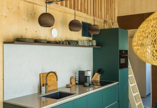 Cocina moderna en la lodge Unbrick One con armarios verdes, paredes de madera y lámparas colgantes.