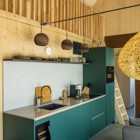 Modern kitchen interior in Unbrick One lodge with green cabinets, wood walls, and hanging pendant lights.