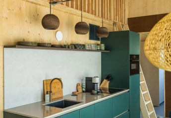 Interno cucina moderna nella lodge Unbrick One con mobili verdi, pareti in legno e lampade a sospensione.