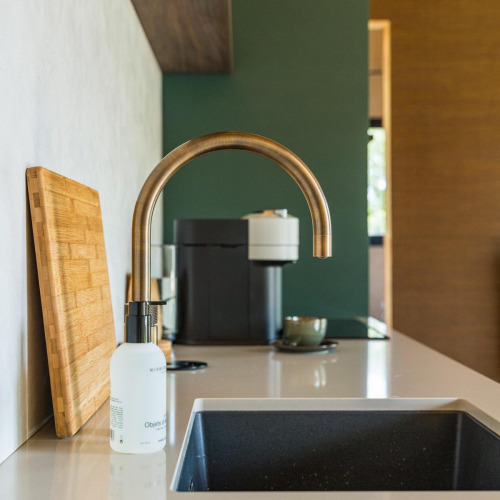 Fregadero de cocina moderno con grifo dorado, tabla de cortar y cafetera en Unbrick One en Países Bajos.