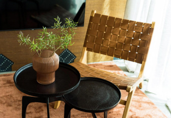 Moderne loungehjørne med flettet læderstol, sorte runde borde og vase med grønne grene i Unbrick One.