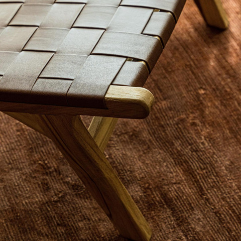 Detail van een geweven houten en leren kruk op bruin tapijt bij Unbrick One lodge, Brinckerduyn.