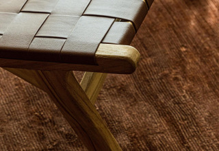 Dettaglio di sgabello intrecciato in legno e pelle su tappeto marrone a Unbrick One lodge, Brinckerduyn.