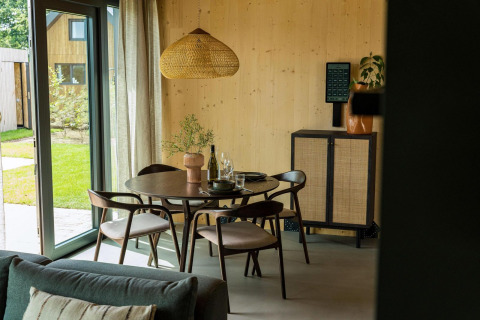 Modern dining area with wooden furniture in Unbrick One lodge at Brinckerduyn, Netherlands, garden view.