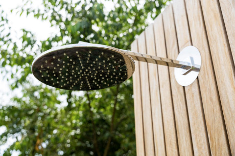 Outdoor shower head mounted on a wooden wall with trees in the background at Brinckerduyn, Netherlands.
