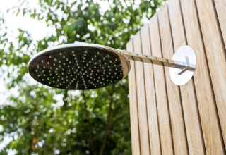 Outdoor shower head mounted on a wooden wall with trees in the background at Brinckerduyn, Netherlands.