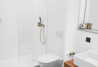 Baño moderno con inodoro suspendido, ducha de lluvia y lavabo de madera en Unbrick One lodge, Países Bajos.