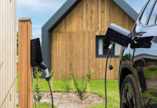Elbil oplades ved Unbrick One-lodge i Brinckerduyn, Nederlandene, med træhus i baggrunden.