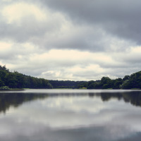 Lago sereno circondato da boschi sotto un cielo nuvoloso, luogo ideale per il glamping in un parco vacanze.