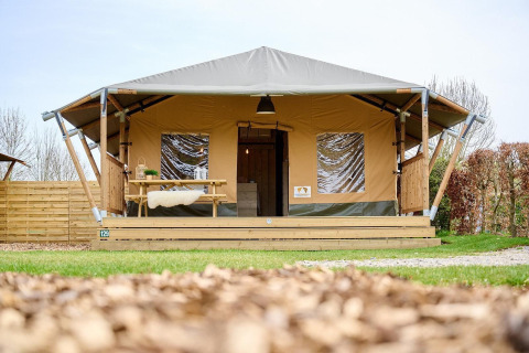 Tienda Safari Cottage en Camping Vossenberg, Países Bajos, vista desde el frente con porche de madera.