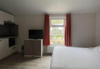 Helles Zimmer in Comfort Lodge mit Doppelbett, Fernseher, Fenster mit roten Vorhängen und Küchenzeile.