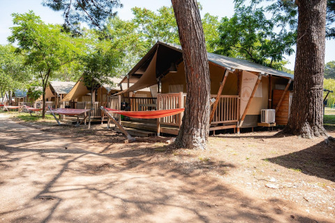 Safari tents with wooden decks and hammocks at Villatent Outback in Bi Village, Croatia, surrounded by trees.
