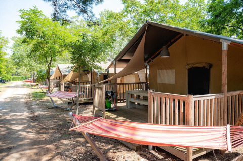 Safari tents with wooden porches and hammocks at Bi Village in Croatia, shaded by green trees and nature.