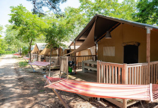 Safari tents with wooden porches and hammocks at Bi Village in Croatia, shaded by green trees and nature.