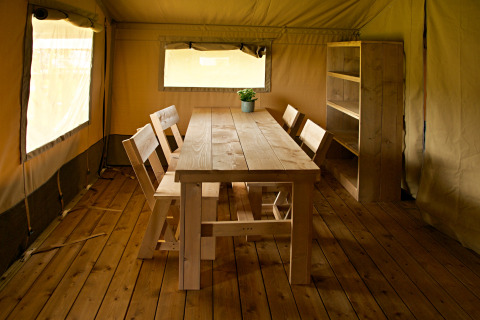 Indvendigt i en safaritelte på Rosenvold Strand Camping, Danmark, med træbord, stole og reol.