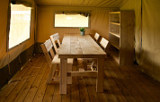 Interior de una tienda safari en Rosenvold Strand Camping, Dinamarca, con mesa, sillas y estantería de madera.
