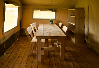 Indvendigt i en safaritelte på Rosenvold Strand Camping, Danmark, med træbord, stole og reol.