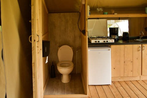 Indvendigt billede af et safaritelt med et toilet, lille køkken, gaskomfur, kaffemaskine og minikøleskab.