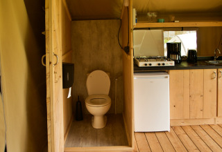 Indvendigt billede af et safaritelt med et toilet, lille køkken, gaskomfur, kaffemaskine og minikøleskab.