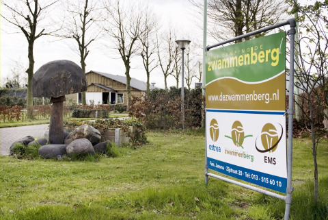 Ingang van Camping de Zwammenberg in Noord-Brabant met bord, houten paddenstoel en vakantiehuisje.