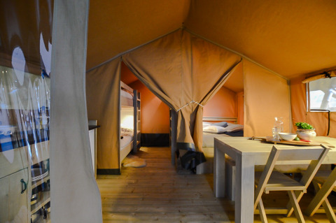 Intérieur d'une tente safari avec lits superposés, table en bois et ambiance chaleureuse et confortable.