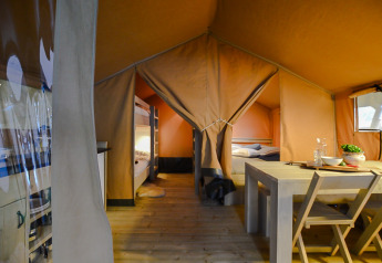 Interno di una tenda safari con letti a castello, tavolo da pranzo in legno e atmosfera accogliente.