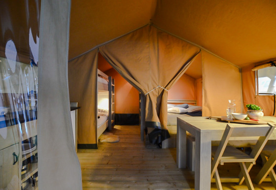 Intérieur d'une tente safari avec lits superposés, table en bois et ambiance chaleureuse et confortable.