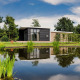 Moderne tiny house ved en dam i Vakantiepark Hölte, Holland, omgivet af grønt og blå himmel.