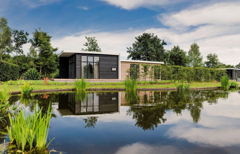 Modernes Ferienhaus mit Hot Tub am Teich im Vakantiepark Hölte, Niederlande, umgeben von üppiger Natur.