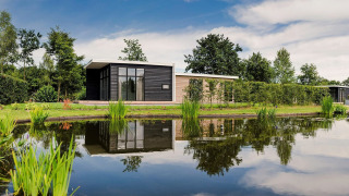 Lodge moderno con vasca idromassaggio presso un laghetto al Vakantiepark Hölte, Paesi Bassi, immerso nel verde.