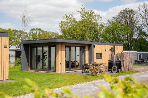 Modern Oak Lodge with hot tub at Vakantiepark Hölte in the Netherlands, set amidst lush greenery.