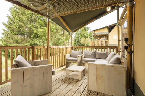 Gezellig terras bij Ranger Lodge safaritent met houten zitbanken, grijze kussens en boszicht.