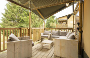Gemütliche Terrasse des Ranger Lodge Safari-Zeltes mit Holzmöbeln, grauen Kissen und Waldblick.