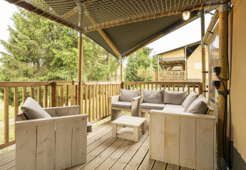 Cozy terrace of Ranger Lodge safari tent with wooden seating, grey cushions, and forest view.