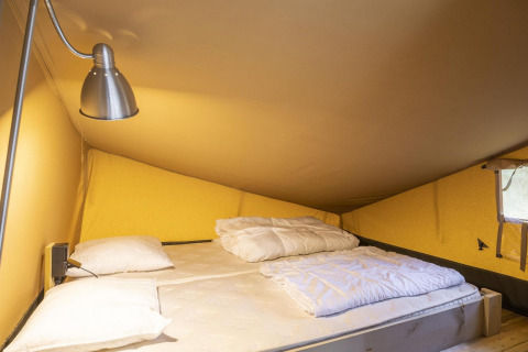 Zona de descanso en tienda safari Ranger Lodge en Petite Suisse, Bélgica, con cama doble y lámpara.