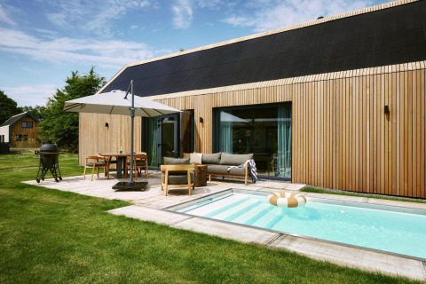 Lodge moderno Unbrick One en De Weelderik, Países Bajos, con piscina, terraza, fachada de madera y muebles al aire libre.