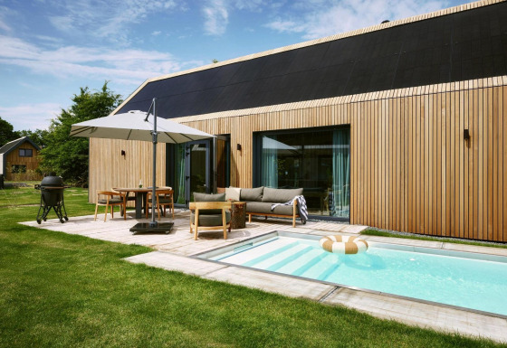 Lodge moderno Unbrick One en De Weelderik, Países Bajos, con piscina, terraza, fachada de madera y muebles al aire libre.
