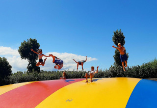 Kinderen springen en spelen op een kleurrijk luchtkussen onder een blauwe hemel bij Kompas Camping Westende.