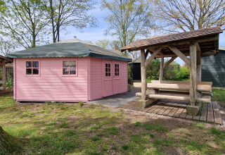 Een roze houten tuinhuisje en een picknicktafel met overkapping bij Zomerlicht vakantiepark in Overijssel.