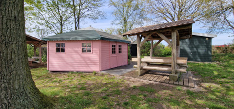 Een roze houten tuinhuisje en een picknicktafel met overkapping bij Zomerlicht vakantiepark in Overijssel.
