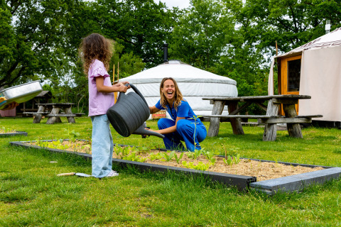 Twee mensen water geven aan planten in een moestuin bij een vakantiepark in Overijssel, Nederland.