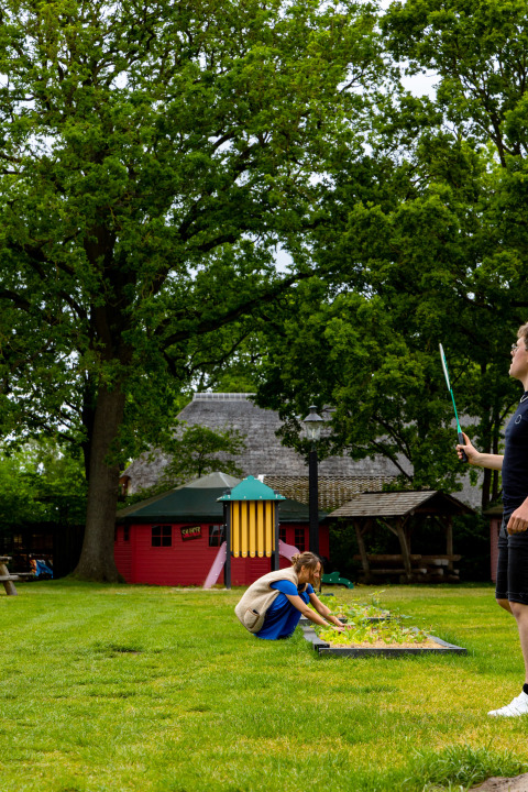 Twee mensen in een groene tuin bij Zomerlicht vakantiepark in Overijssel, Nederland, met bomen op de achtergrond.