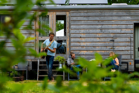 Drie mensen ontspannen bij een houten tiny house in Zomerlicht vakantiepark, Overijssel, Nederland.