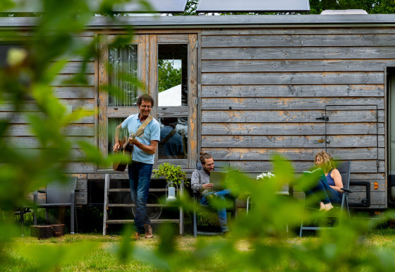 Drie mensen ontspannen bij een houten tiny house in Zomerlicht vakantiepark, Overijssel, Nederland.
