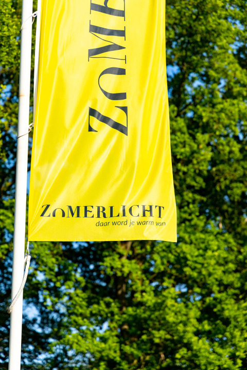 Gele vlag van het vakantiepark Zomerlicht in Overijssel, Nederland, tegen een groene achtergrond.