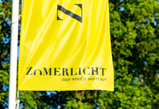 Gele vlag van het vakantiepark Zomerlicht in Overijssel, Nederland, tegen een groene achtergrond.