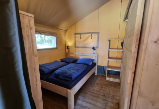 Binnenzicht van een glamping tent met een houten bed, blauwe dekens en een houten vloer in een gezellige sfeer.