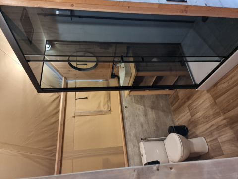 Moderne badkamer in een glampingaccommodatie met glazen douche, toilet en houten afwerking.